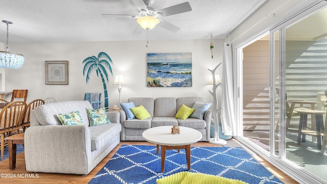 living room featuring a textured ceiling, plenty of natural light, wood finished floors, and ceiling fan with notable chandelier