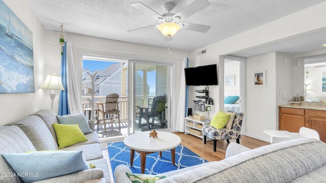 living room featuring a textured ceiling, ceiling fan, visible vents, and light wood-type flooring