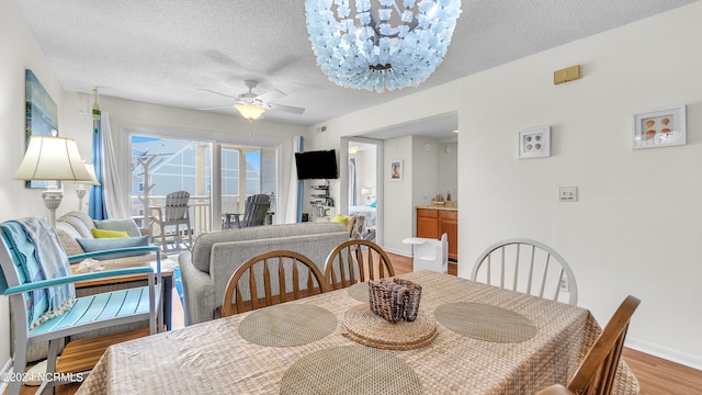 dining area with hardwood / wood-style flooring, ceiling fan with notable chandelier, and a textured ceiling