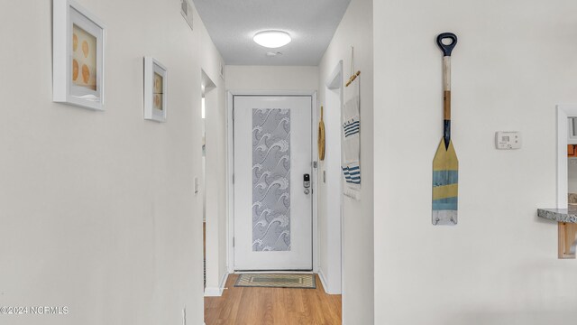 doorway with visible vents, baseboards, a textured ceiling, and wood finished floors