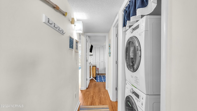 clothes washing area featuring stacked washer and dryer, wood-type flooring, and a textured ceiling