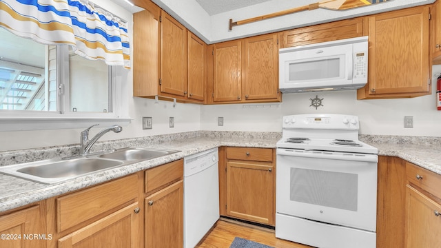 kitchen with brown cabinetry, white appliances, light countertops, a sink, and light wood-style flooring