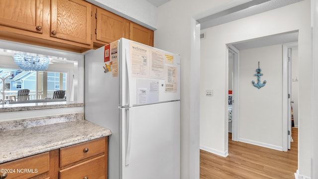 kitchen with an inviting chandelier, freestanding refrigerator, baseboards, light countertops, and light wood finished floors