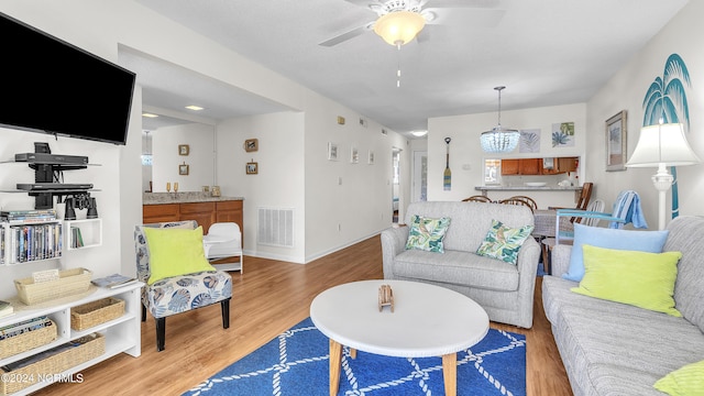 living area featuring visible vents, baseboards, ceiling fan with notable chandelier, and wood finished floors