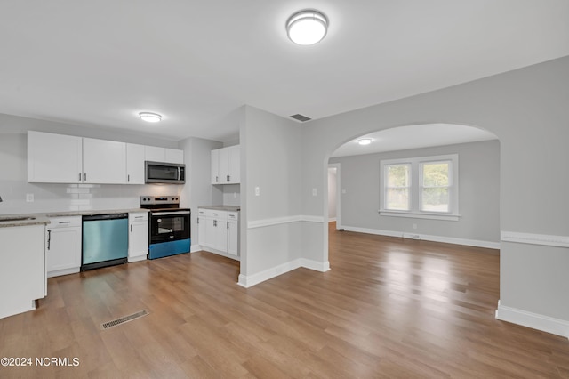 kitchen featuring baseboards, arched walkways, a sink, light wood finished floors, and stainless steel appliances