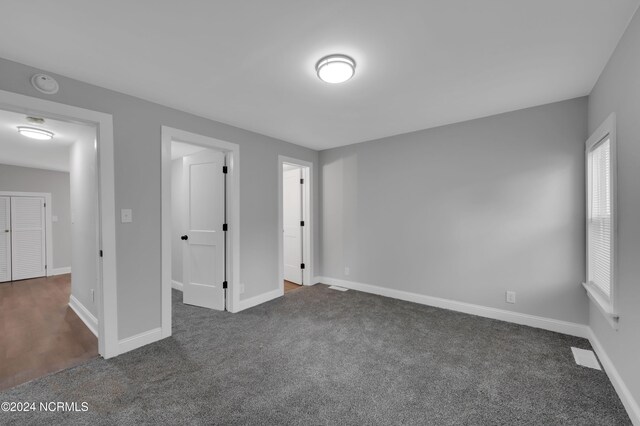 unfurnished bedroom featuring baseboards, dark colored carpet, and visible vents