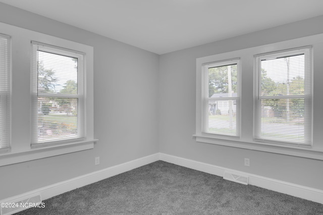 spare room with baseboards, dark colored carpet, and visible vents
