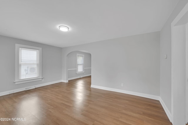 empty room featuring arched walkways, plenty of natural light, and wood finished floors