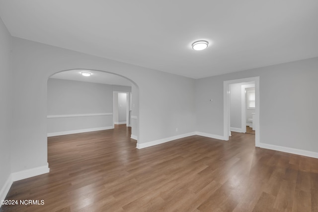 unfurnished room with baseboards, arched walkways, and wood finished floors
