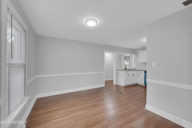 unfurnished living room featuring visible vents, a sink, light wood-style flooring, and baseboards