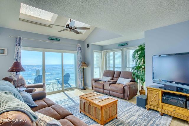 living room with vaulted ceiling with skylight, hardwood / wood-style floors, a textured ceiling, and ceiling fan