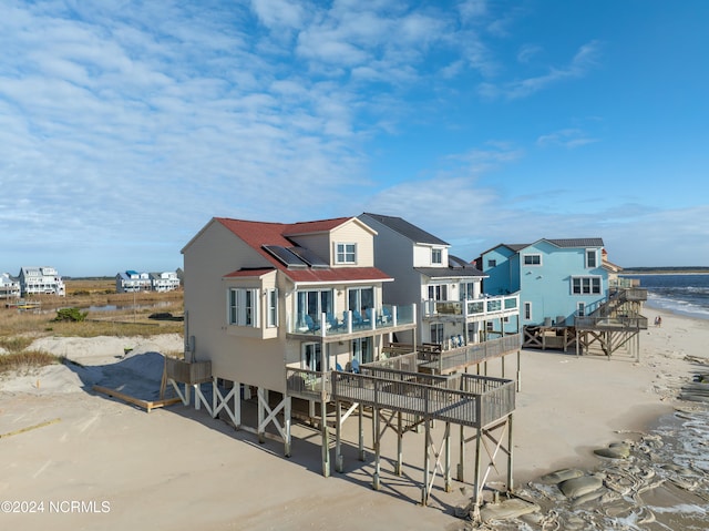 rear view of house with a view of the beach, a water view, and a balcony