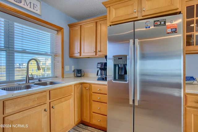 kitchen featuring light brown cabinets, stainless steel fridge, sink, and a textured ceiling