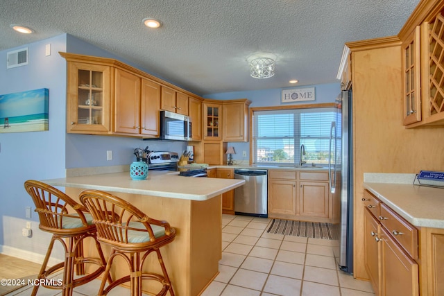 kitchen with appliances with stainless steel finishes, a textured ceiling, kitchen peninsula, a kitchen breakfast bar, and light tile patterned floors