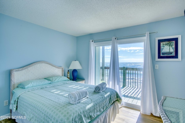 bedroom featuring a water view, access to outside, a textured ceiling, and light wood-type flooring