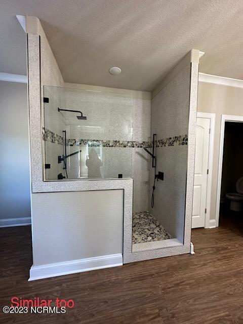 bathroom featuring ornamental molding, tiled shower, wood-type flooring, and a textured ceiling