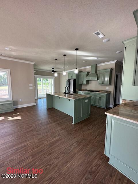 kitchen with dark wood-type flooring, a healthy amount of sunlight, wall chimney range hood, and decorative light fixtures