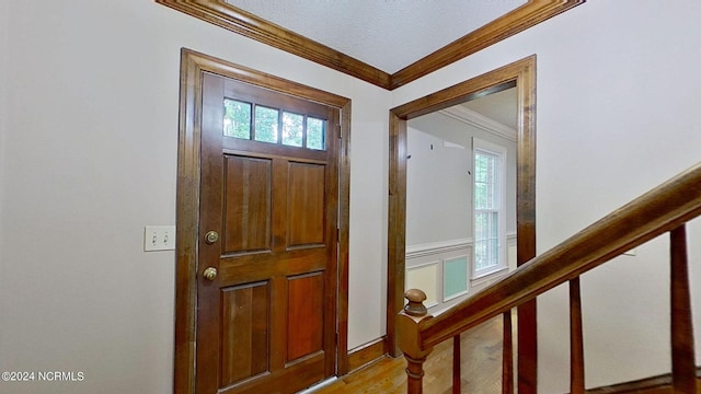 entrance foyer with a textured ceiling, light hardwood / wood-style flooring, ornamental molding, and a wealth of natural light