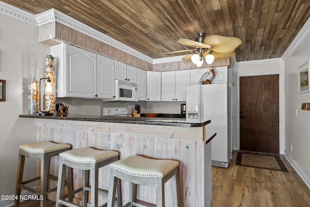 kitchen with white appliances, a peninsula, crown molding, dark countertops, and white cabinetry