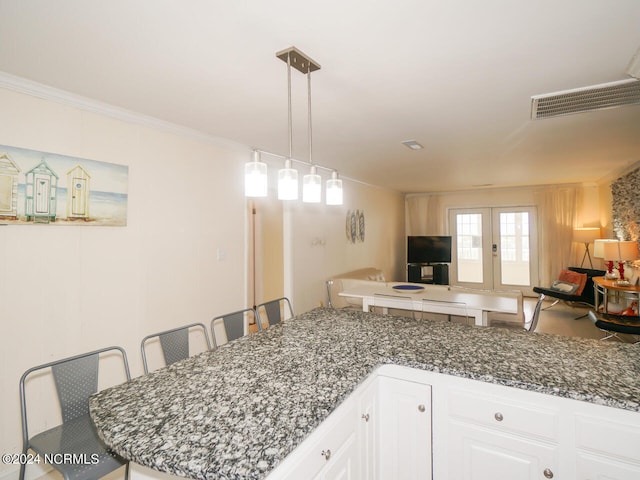 kitchen with white cabinets, a kitchen bar, crown molding, dark stone countertops, and french doors