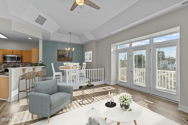 living room featuring plenty of natural light, light hardwood / wood-style floors, a raised ceiling, and ceiling fan with notable chandelier