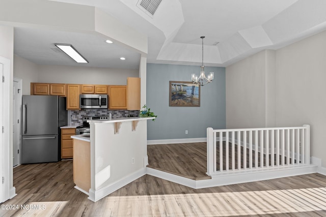 kitchen featuring a kitchen breakfast bar, decorative backsplash, light wood-type flooring, decorative light fixtures, and stainless steel appliances