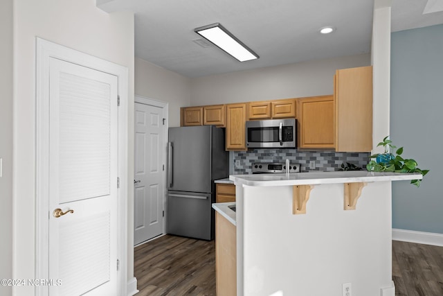 kitchen with a kitchen breakfast bar, kitchen peninsula, dark wood-type flooring, and appliances with stainless steel finishes