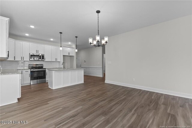 kitchen with dark wood-type flooring, white cabinets, a center island with sink, decorative light fixtures, and stainless steel appliances