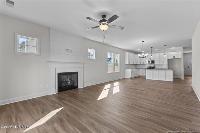 unfurnished living room with ceiling fan with notable chandelier, hardwood / wood-style floors, and a large fireplace