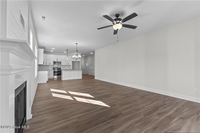 unfurnished living room with sink, ceiling fan with notable chandelier, and dark hardwood / wood-style floors