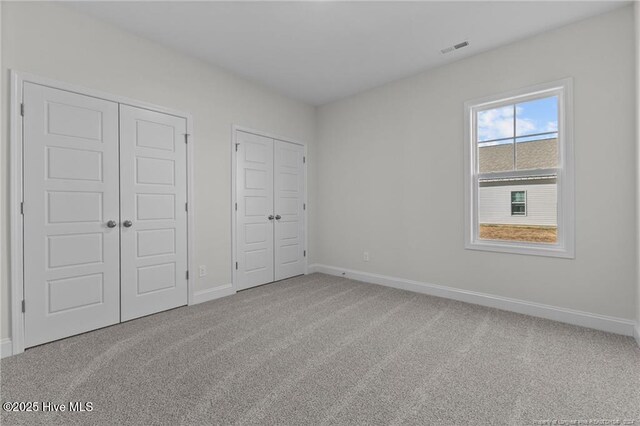 unfurnished bedroom featuring carpet flooring and multiple closets