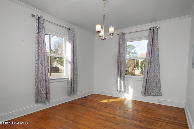 empty room with ornamental molding, a wealth of natural light, visible vents, and hardwood / wood-style flooring