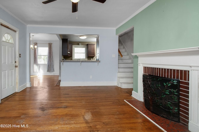 unfurnished living room with stairway, ornamental molding, a fireplace with raised hearth, and wood finished floors