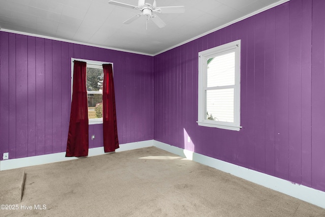 empty room featuring carpet, crown molding, baseboards, and a ceiling fan