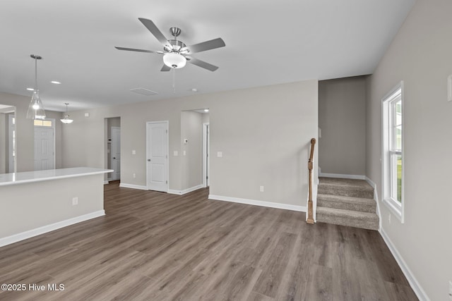 unfurnished living room featuring baseboards, stairway, ceiling fan, and wood finished floors