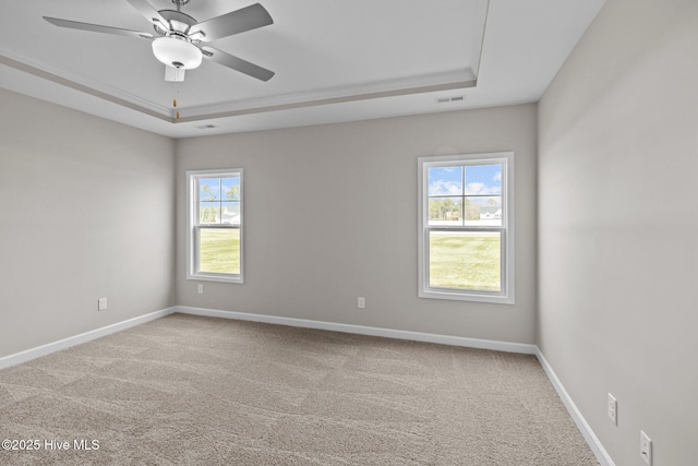 carpeted empty room featuring visible vents, baseboards, a raised ceiling, and a wealth of natural light