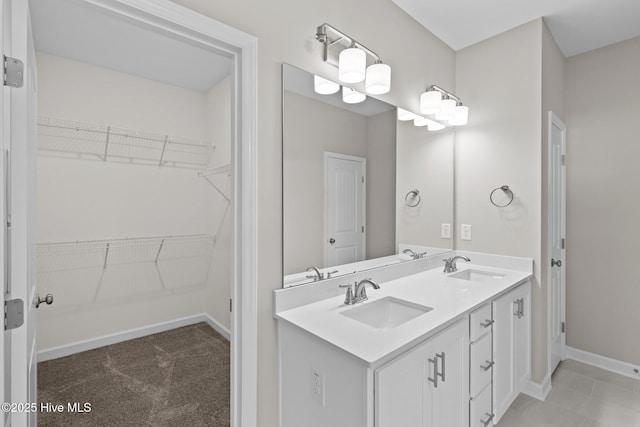 bathroom with double vanity, a spacious closet, baseboards, and a sink