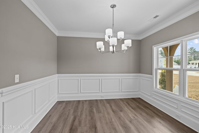 unfurnished dining area with a chandelier, dark wood-style flooring, wainscoting, and crown molding