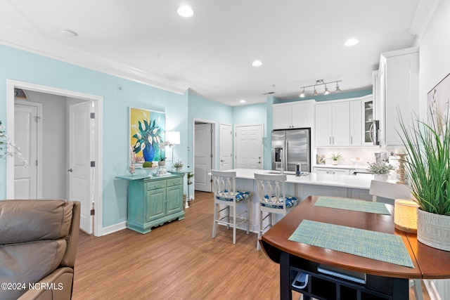 kitchen featuring stainless steel appliances, tasteful backsplash, white cabinets, light hardwood / wood-style flooring, and ornamental molding