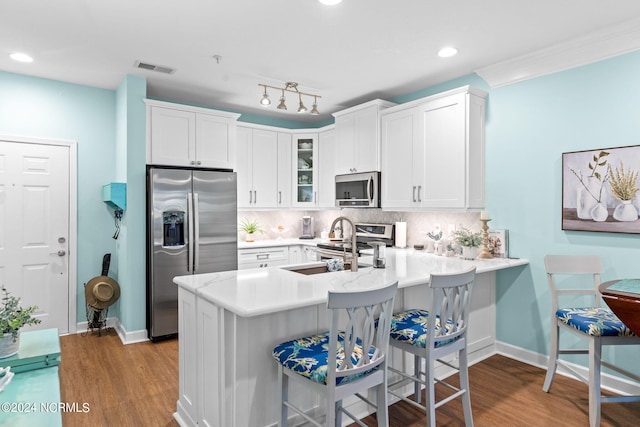 kitchen featuring decorative backsplash, light hardwood / wood-style floors, kitchen peninsula, white cabinetry, and appliances with stainless steel finishes