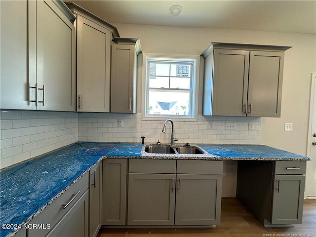 kitchen with decorative backsplash, dark stone counters, sink, gray cabinets, and light hardwood / wood-style floors