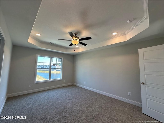 unfurnished room with a raised ceiling, carpet floors, ceiling fan, a water view, and ornamental molding