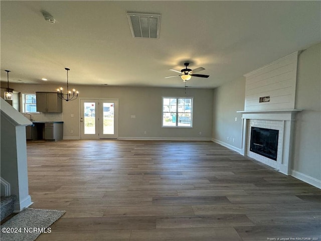 unfurnished living room featuring sink, ceiling fan with notable chandelier, a fireplace, and dark hardwood / wood-style flooring