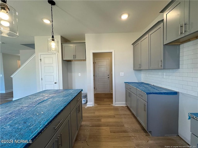 kitchen with hanging light fixtures, gray cabinetry, backsplash, dark stone counters, and dark hardwood / wood-style flooring