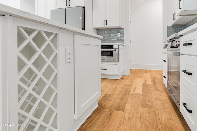 kitchen featuring backsplash, light hardwood / wood-style flooring, white cabinetry, and stainless steel oven