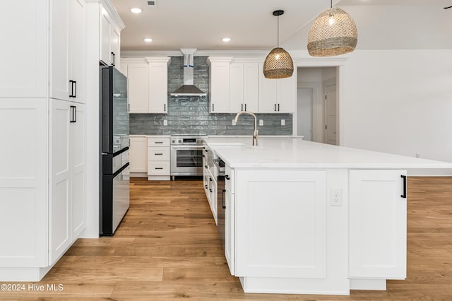 kitchen with light hardwood / wood-style flooring, wall chimney exhaust hood, decorative light fixtures, white cabinetry, and stainless steel appliances