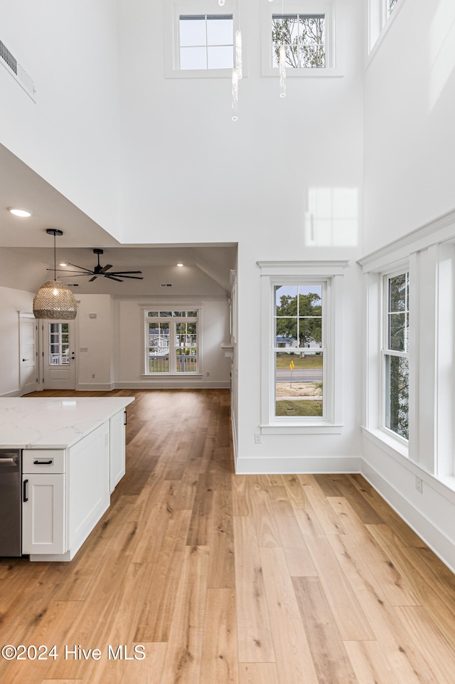 unfurnished living room with ceiling fan, a high ceiling, and light hardwood / wood-style flooring