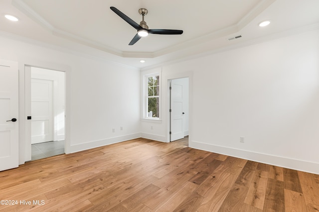 unfurnished bedroom featuring a tray ceiling, crown molding, ceiling fan, and light hardwood / wood-style floors