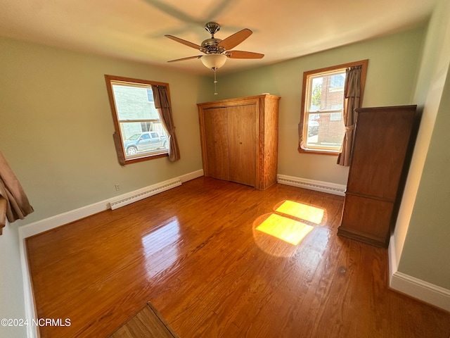 unfurnished bedroom with wood-type flooring, baseboard heating, and ceiling fan