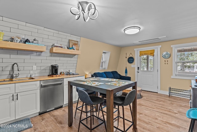 kitchen with stainless steel dishwasher, open shelves, a sink, and light wood-style floors